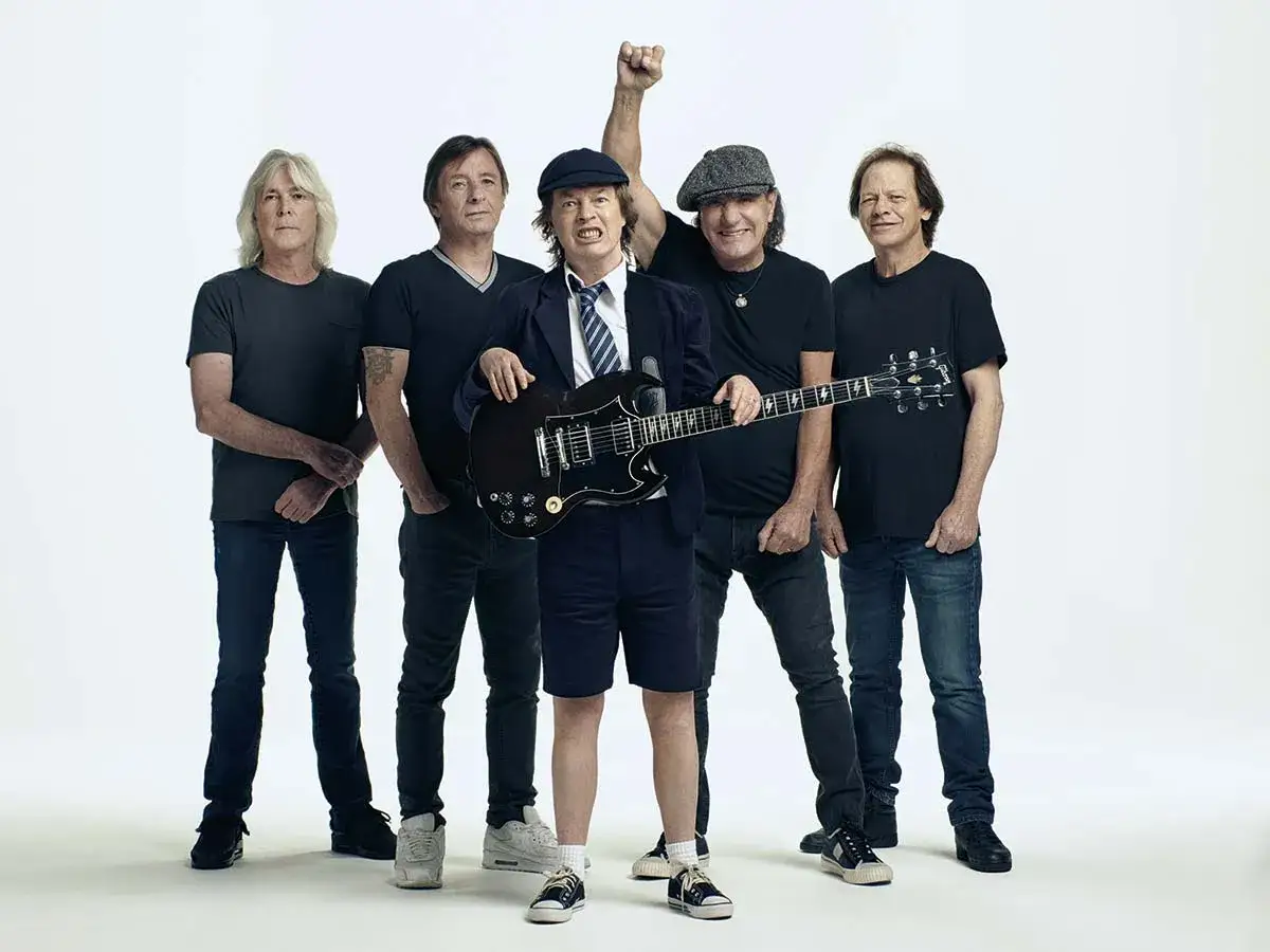 F&uuml;nf M&auml;nner posieren f&uuml;r ein Foto, einer h&auml;lt eine Gitarre. Sie repr&auml;sentieren die legend&auml;re ACDC Musikrichtung.