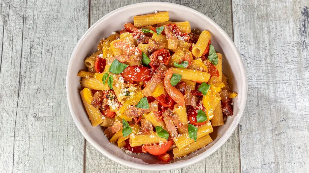 Piatto di pasta con peperoni, pomodorini, basilico e formaggio grattugiato, un classico saporito.