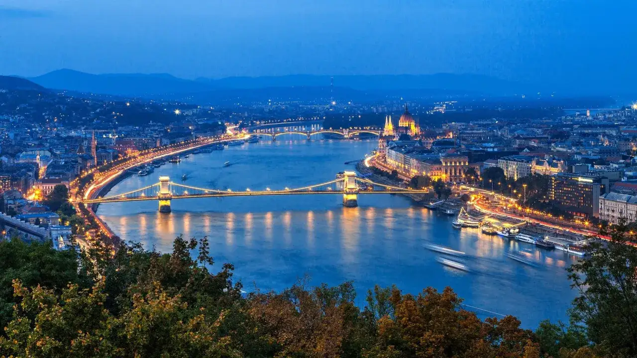 Nocny widok na Dunaj i oświetlone mosty w Budapeszcie. W oddali widać Parlament, a na pierwszym planie drzewa. To magiczne budapeszt stare miasto.
