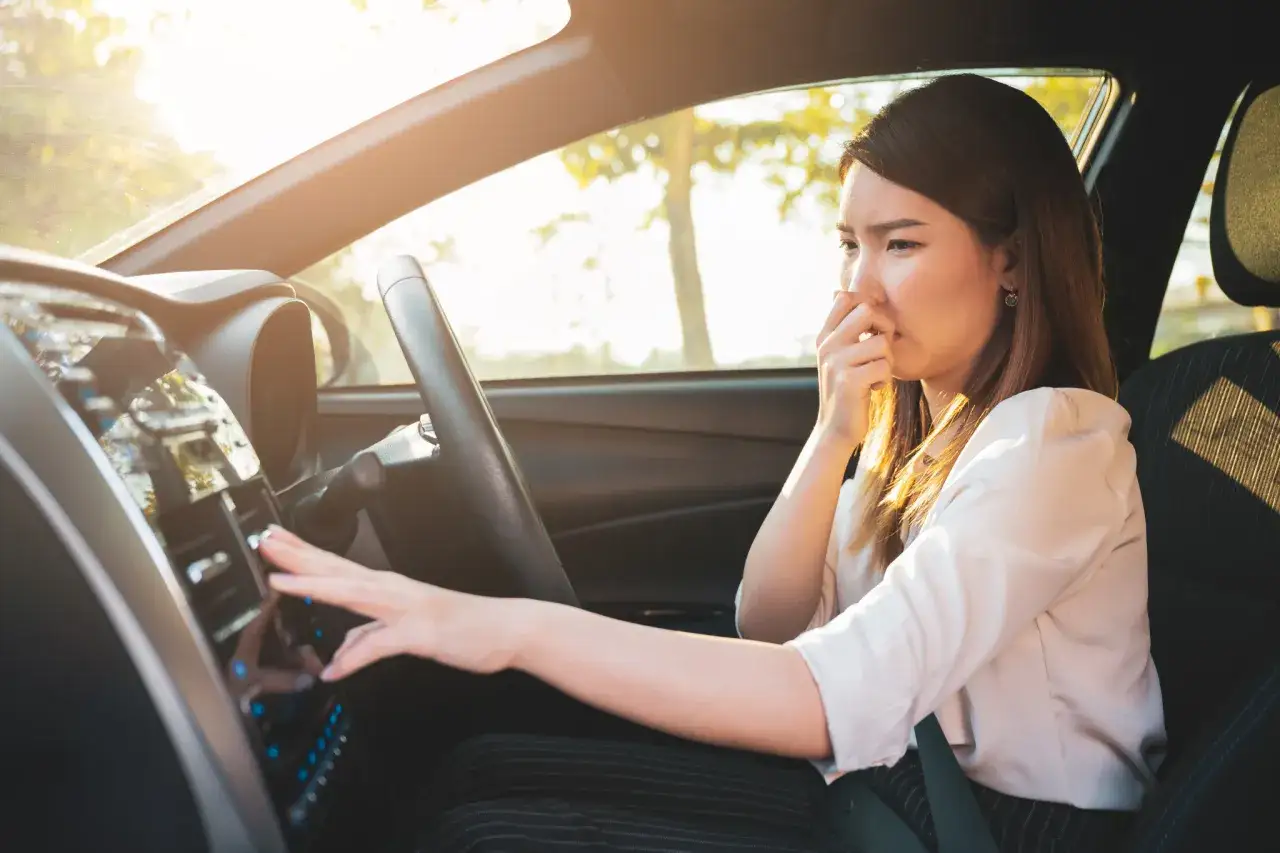 Frau im Auto hält sich die Nase zu, weil das Auto nach Benzin riecht. Sie versucht, die Lüftung einzustellen.