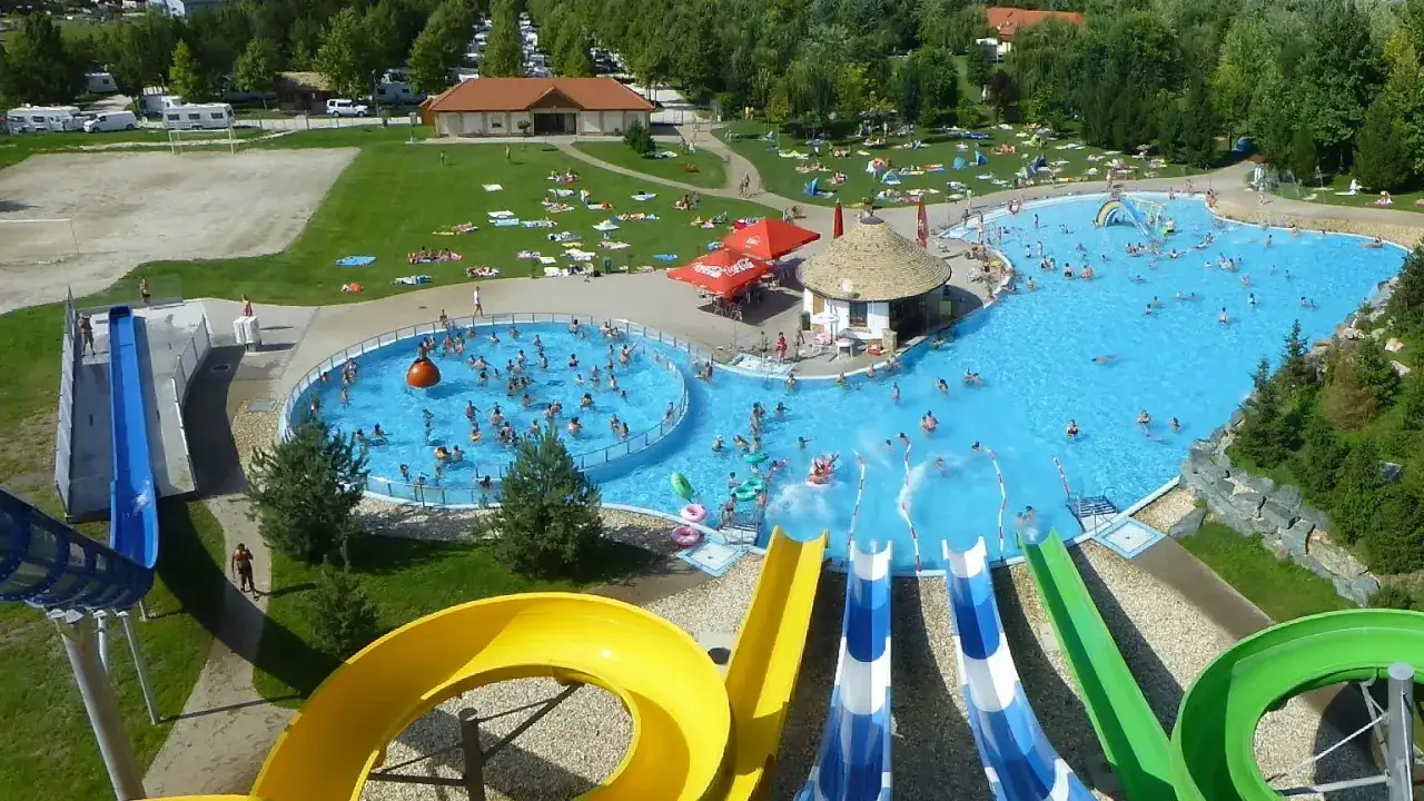 Wesoły tłum ludzi korzysta z basenów i zjeżdżalni w **lipot camping**. Słońce świeci, a woda zaprasza do zabawy.