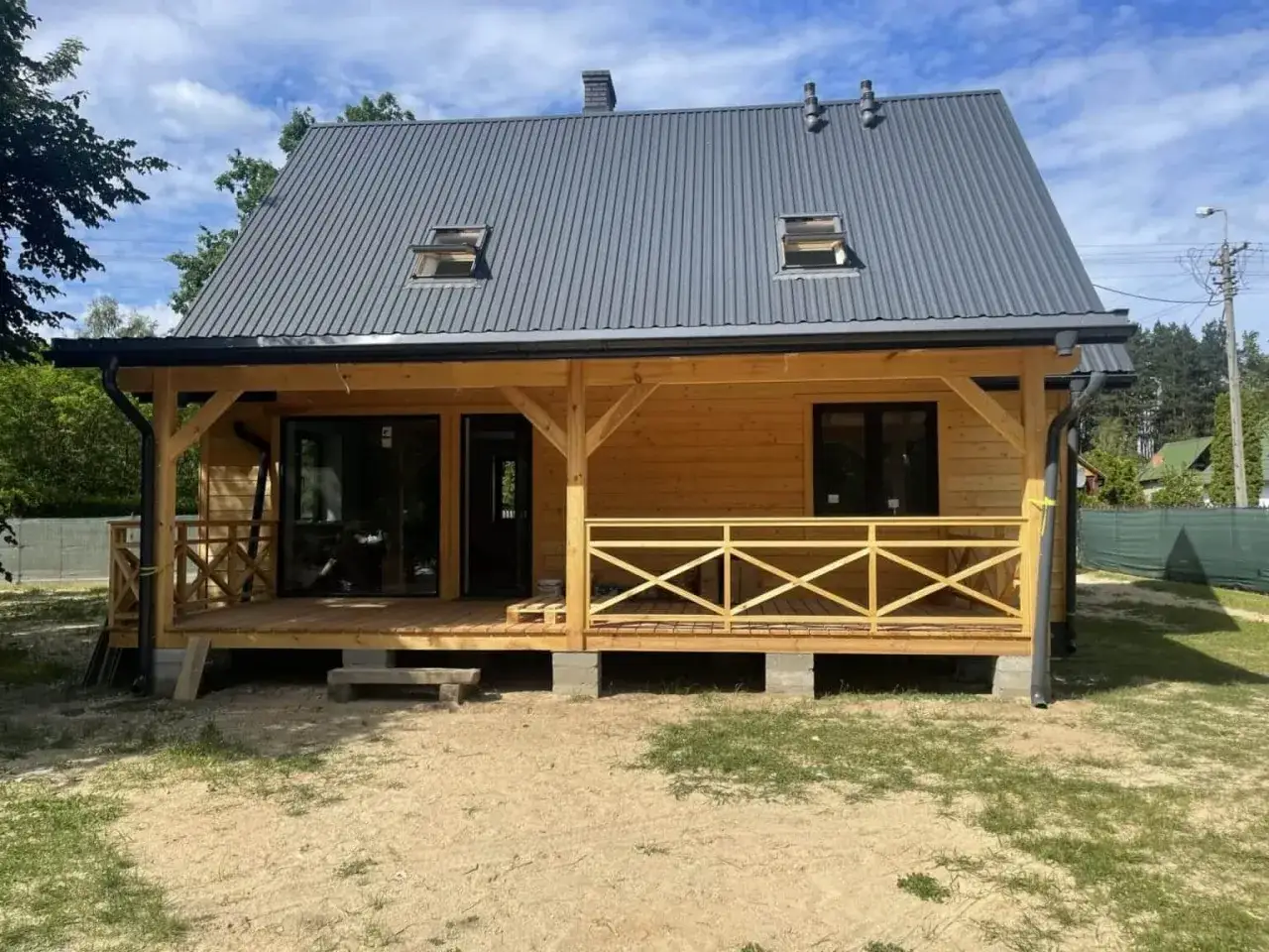 Nowy dom z bali, przykład budownictwa drewnianego w Polsce. Drewniana weranda i dach z blachy.