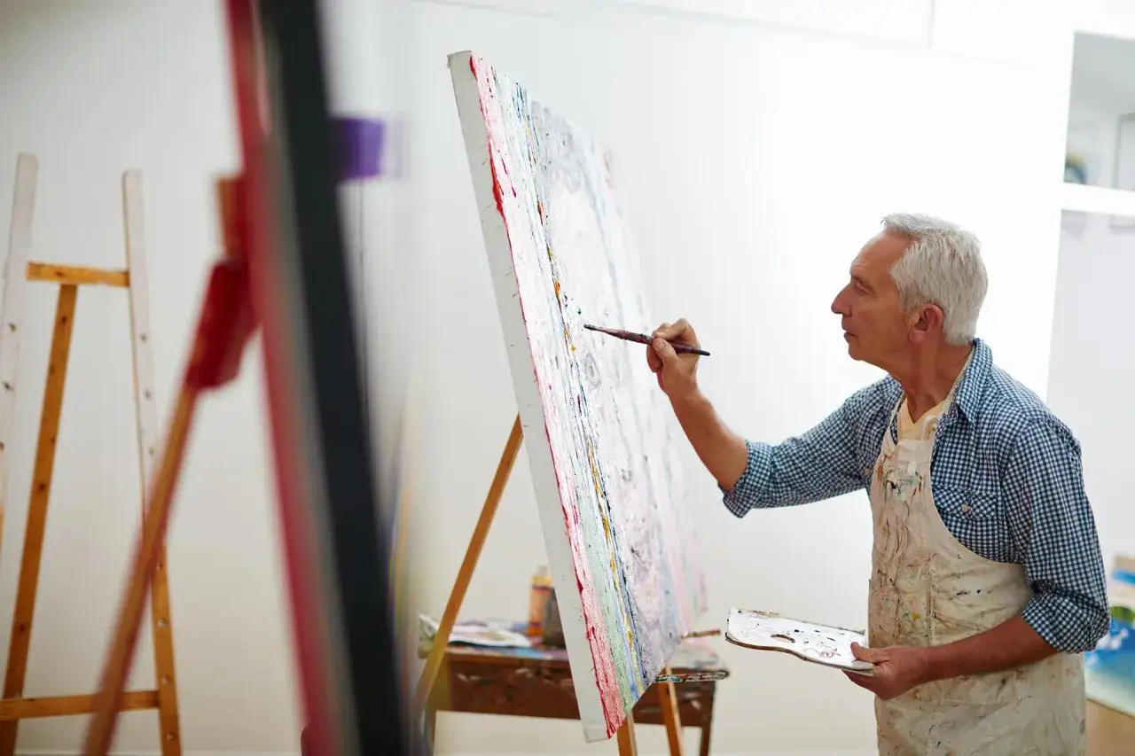 Un artiste peintre, profitant de sa retraite, crée une œuvre colorée. Son activité artistique est une passion.