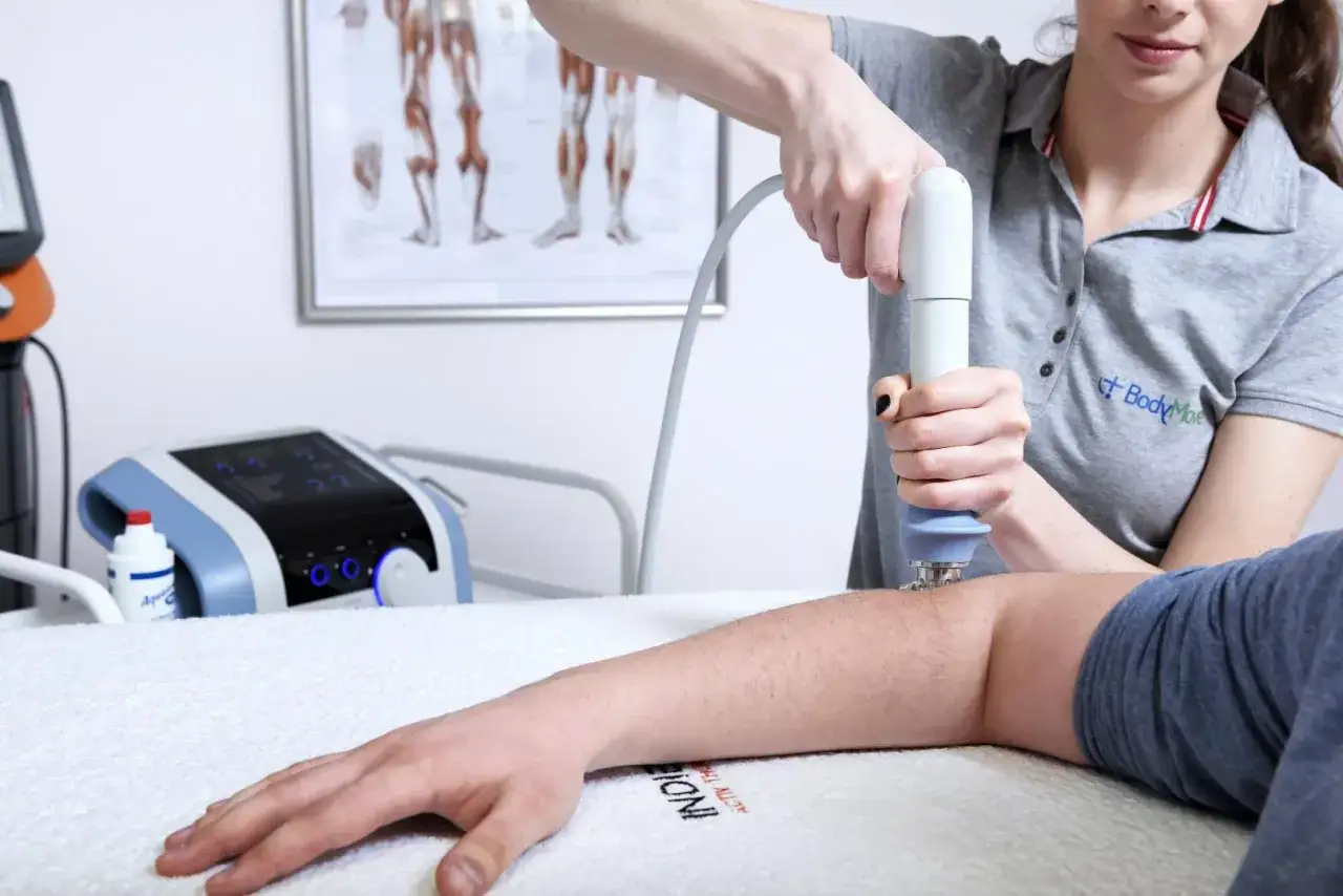Fizjoterapeuta aplikuje falę uderzeniową na przedramię pacjenta, wspomagając regenerację.
