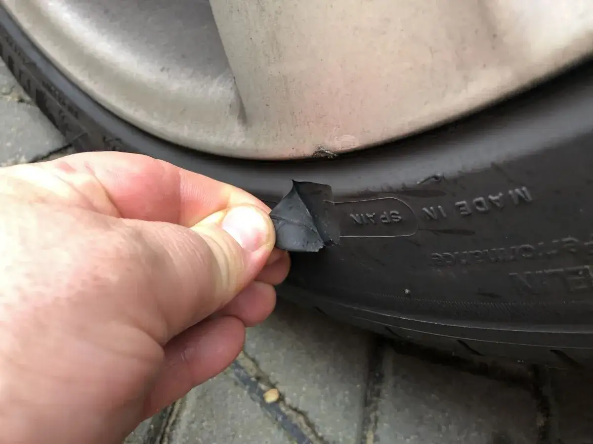 Dłoń odrywa kawałek gumy z boku opony, ukazując pęknięcia.