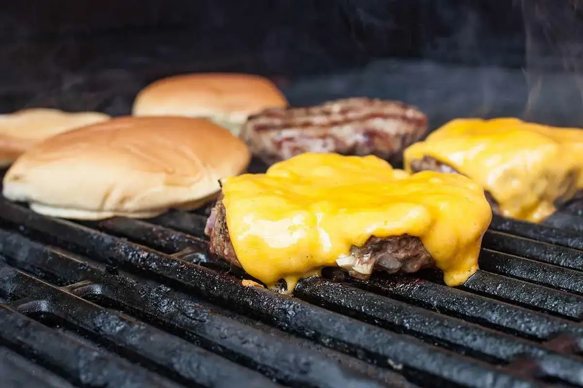 Hamburgers au barbecue, avec du fromage fondant dégoulinant sur les steaks. Des pains à hamburger sont prêts à être assemblés.