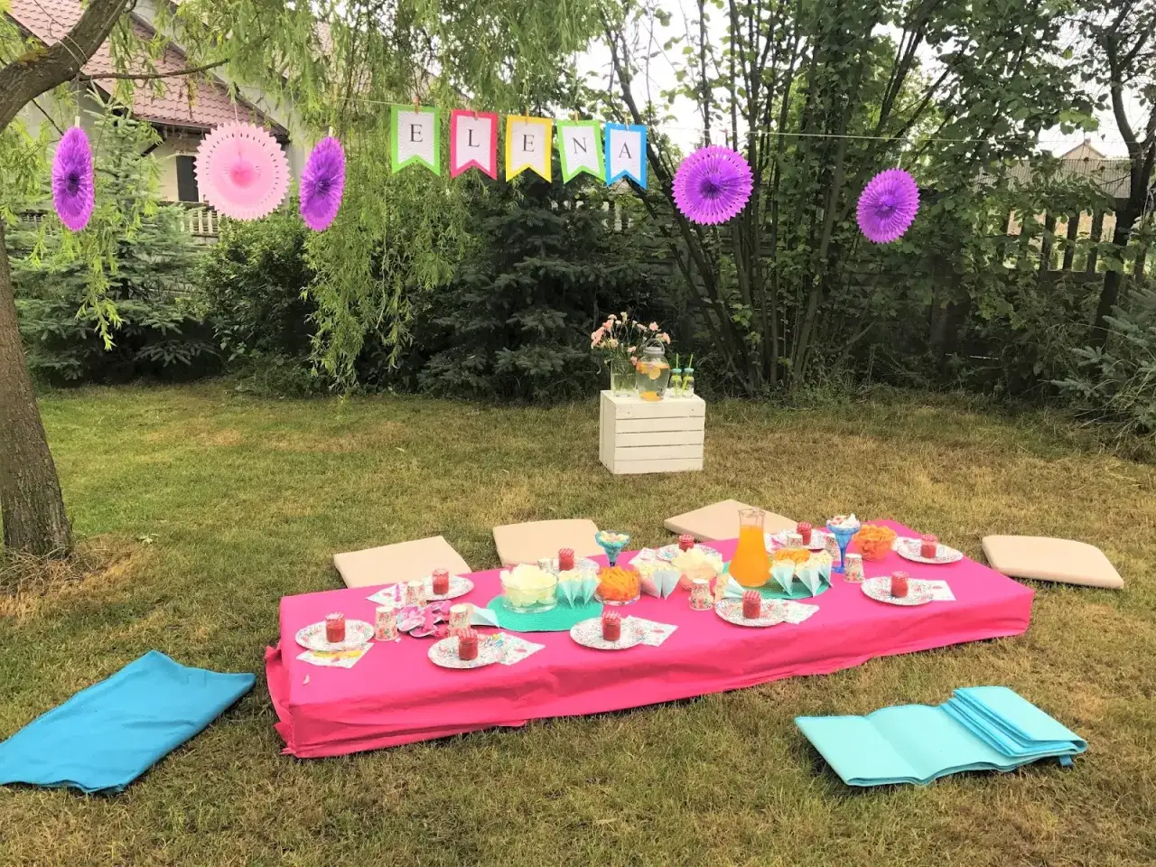 Kolorowy ogród gotowy na urodziny dla 7 latka! Stół z poczęstunkiem, girlanda z imieniem i balony tworzą radosną atmosferę.