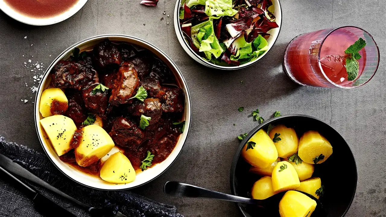 Zartes Gulasch mit Kartoffeln, Salat und einem roten Getr&auml;nk. So wird Gulasch zart: langes Schmoren!