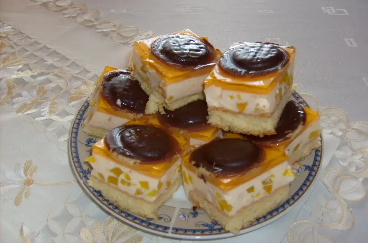 Pyszne ciasto z delicjami, z warstwą biszkoptu, kremu, owoców i galaretki, ozdobione czekoladowym ciastkiem.