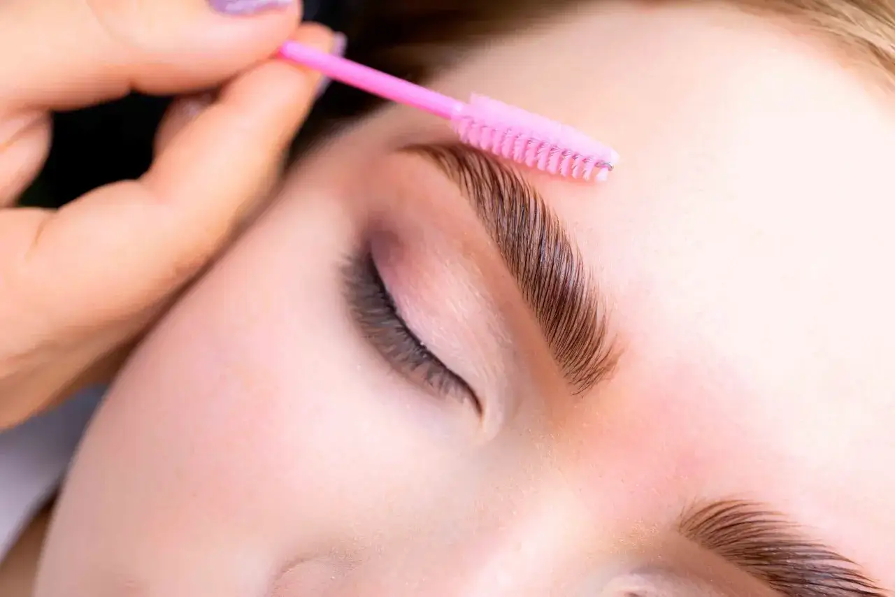 Manos peinan cejas laminadas con cepillo rosa. El laminado de cejas dura semanas, &iexcl;un look perfecto!