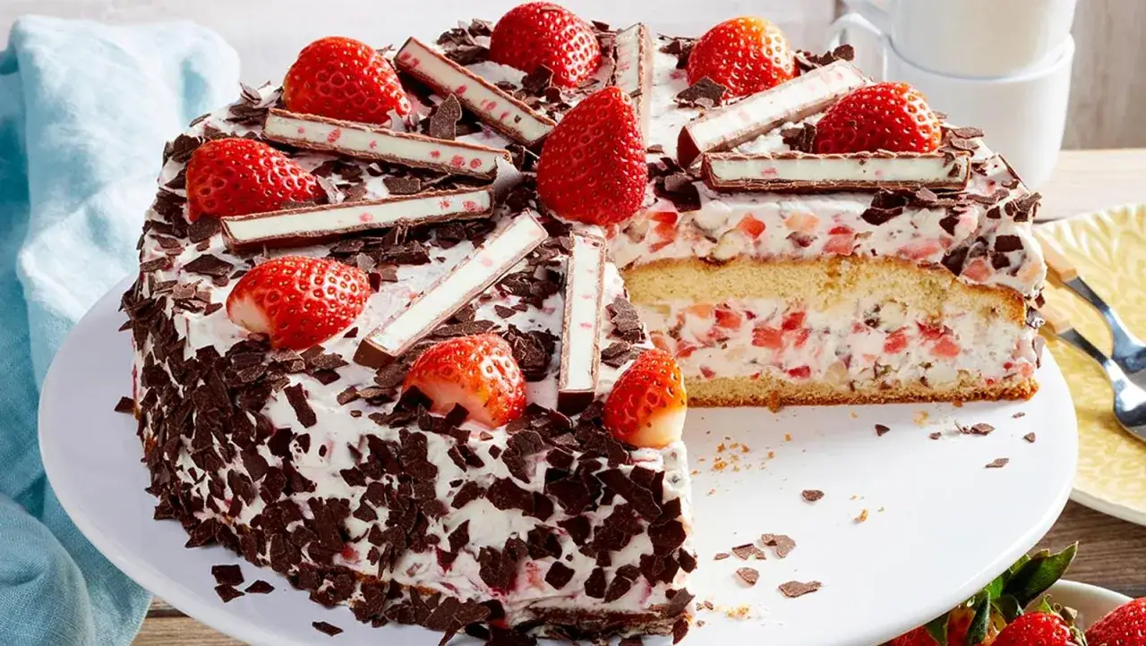Eine k&ouml;stliche Yogurette Torte mit frischen Erdbeeren, Schokost&uuml;ckchen und Sahne. Ein St&uuml;ck ist bereits angeschnitten.