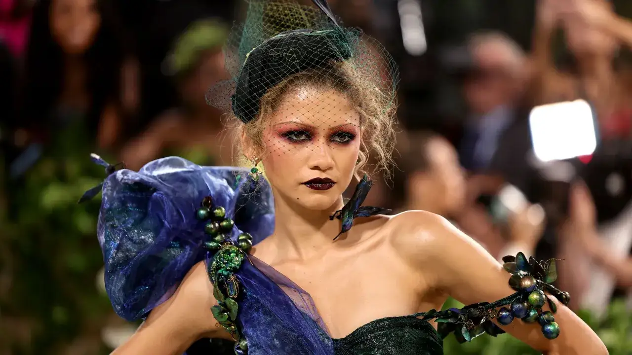 Zendaya deslumbrante en la Met Gala, con un vestido verde oscuro y velo, luciendo un maquillaje dramático y joyas inspiradas en la naturaleza.