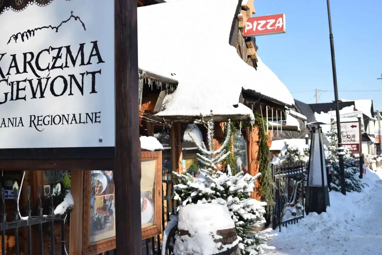 Karczma Giewont w Bukowinie Tatrzańskiej oferuje tanie jedzenie. Zimą budynek pokryty jest śniegiem, a obok widać znak 