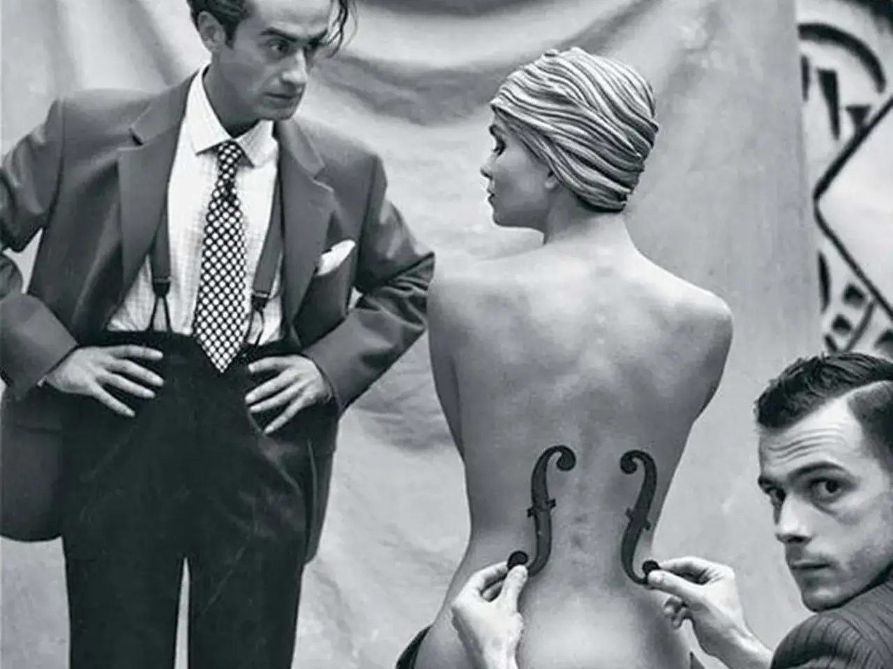 L'iconica **solarizzazione Man Ray** con due f-hole di violino applicati sulla schiena di una modella, mentre un uomo in abito la osserva.