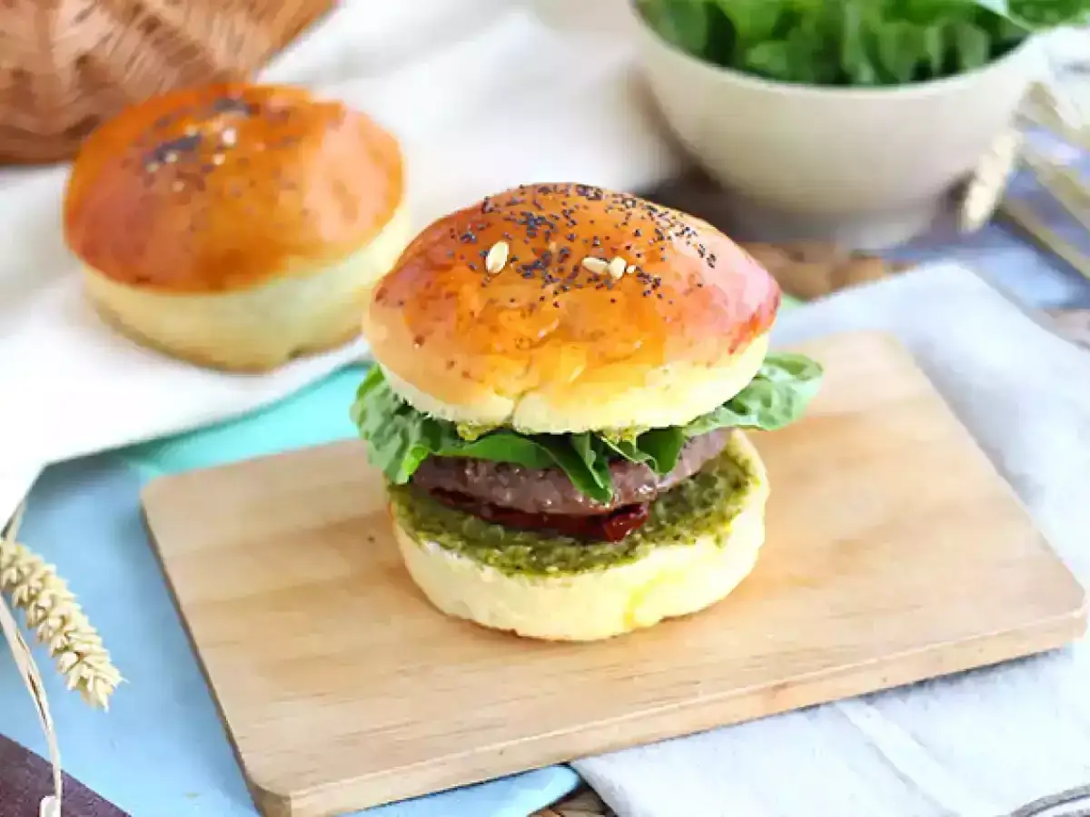 Pyszny burger włoski z zielonym pesto i soczystą wołowiną, podany na drewnianej desce.