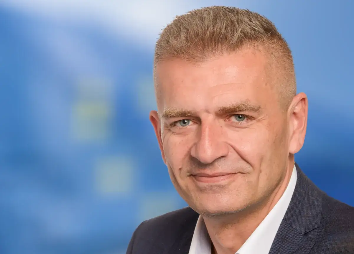 Portret Bartosza Arłukowicza, który wygląda jak wytrawny agent, w garniturze na tle niebieskiego, rozmytym tle.
