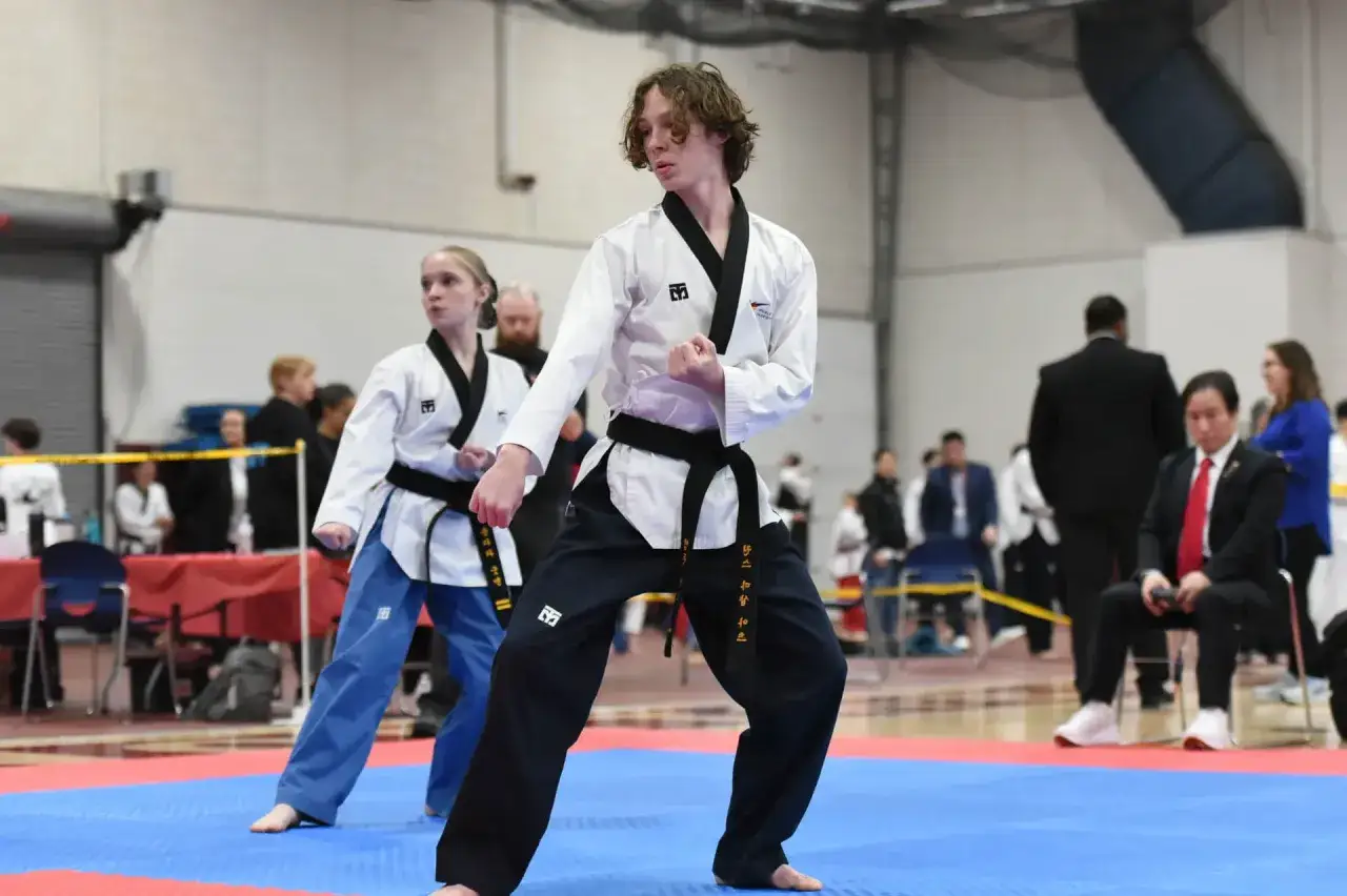 Två unga utövare i tae kwon do, en kille och en tjej, står redo på mattan.