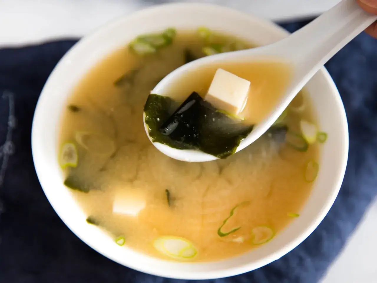 A spoonful of warm miso sauce soup, with tofu, seaweed, and green onions, ready to be enjoyed.