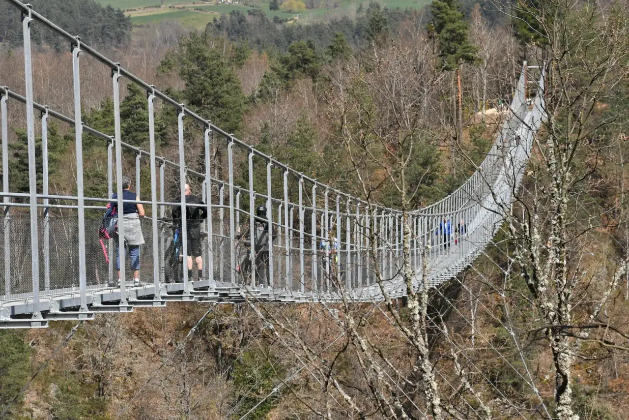 La passerelle himalayenne de Grazac, suspendue au-dessus d'une vall&eacute;e bois&eacute;e, accueille des promeneurs profitant du paysage.