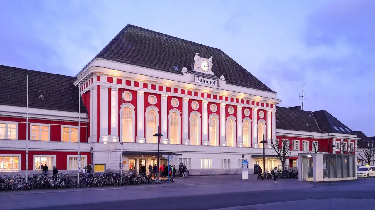 Prachtvoller Bahnhof in Rot und Wei&szlig;, beleuchtet im Abendlicht. Viele Fahrr&auml;der stehen davor. Ein Kandidat f&uuml;r den besten Bahnhof Deutschlands.