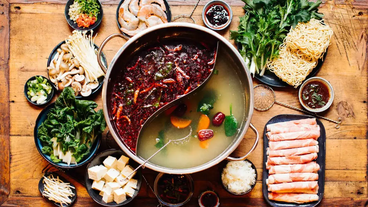 Alles f&uuml;r ein k&ouml;stliches Hot Pot selber machen: Br&uuml;he, Fleisch, Gem&uuml;se, Tofu, Pilze, Garnelen, Nudeln und Dips auf Holztisch.
