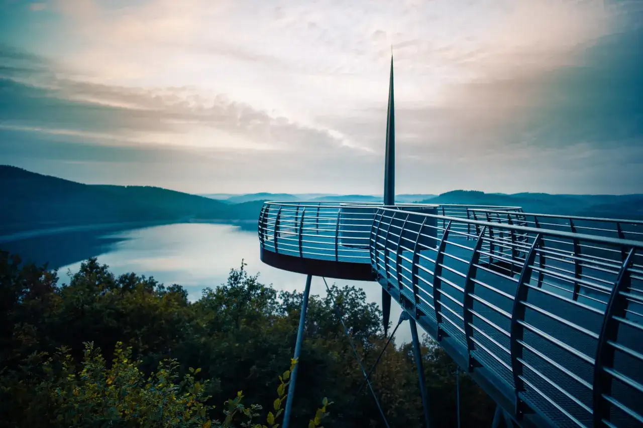 Moderner Skywalk NRW mit Blick auf einen See und sanfte H&uuml;gel im Morgengrauen.
