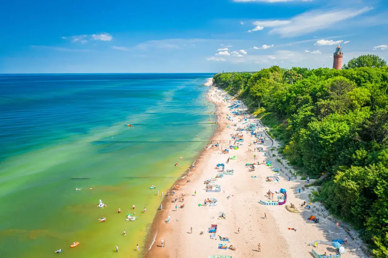 Plaża w Mielnie pełna ludzi, zielony las i charakterystyczna latarnia morska. To idealne miejsce, by sprawdzić, co warto zobaczyć w Mielnie i okolicach.