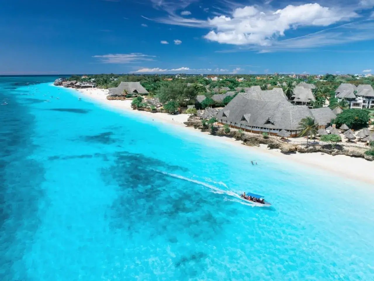 Rajska plaża na Zanzibarze z turkusową wodą i łodzią. Idealne miejsce, by zapytać, kiedy lecieć na Zanzibar.