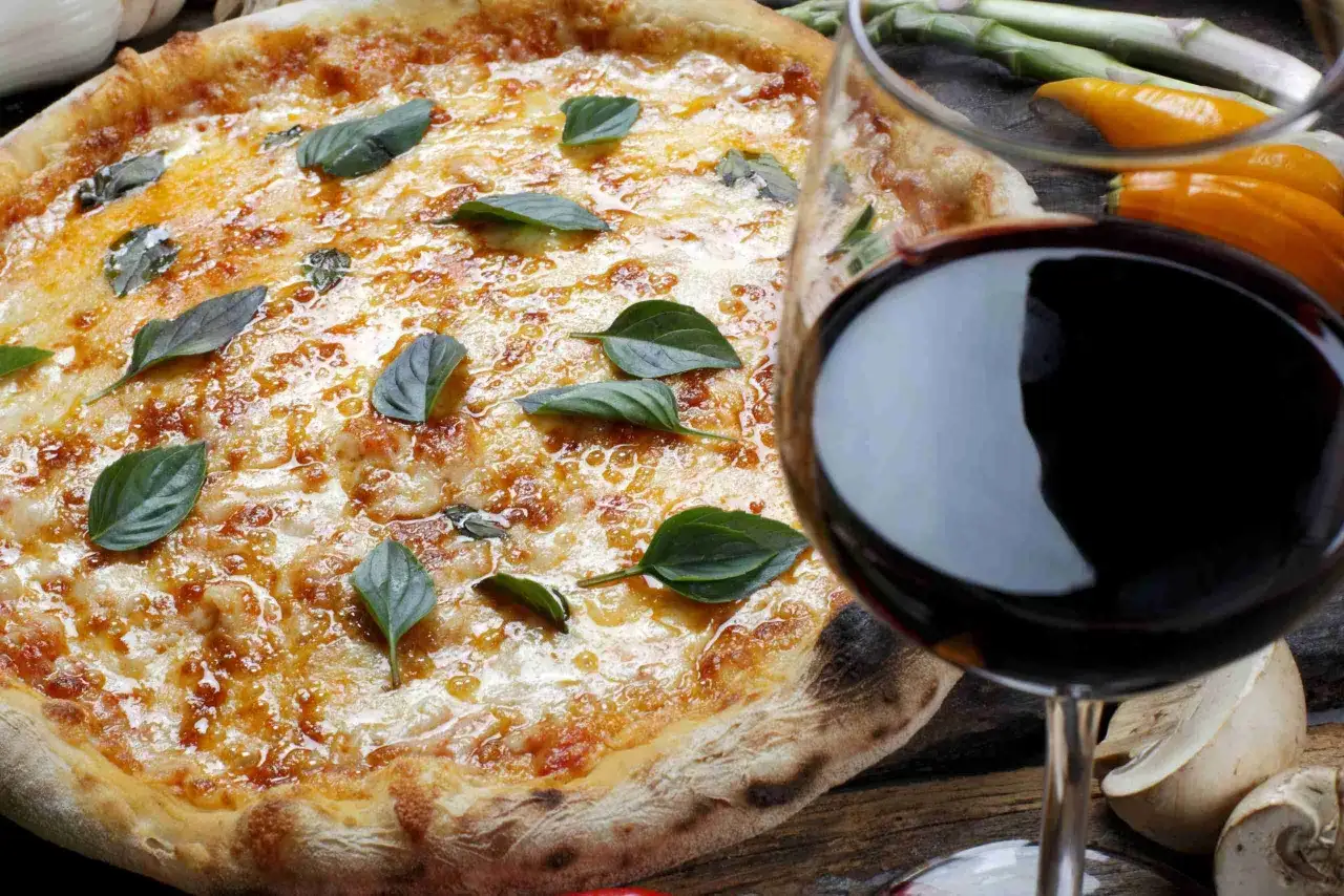Pizza margherita appena sfornata con basilico fresco e un bicchiere di vino rosso, un perfetto abbinamento vino pizza.