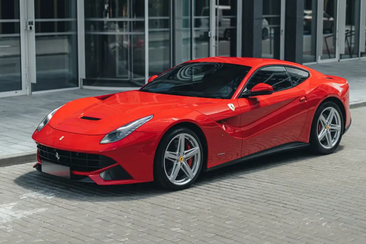 Czerwone Ferrari F12 Berlinetta lśni na tle nowoczesnego budynku.