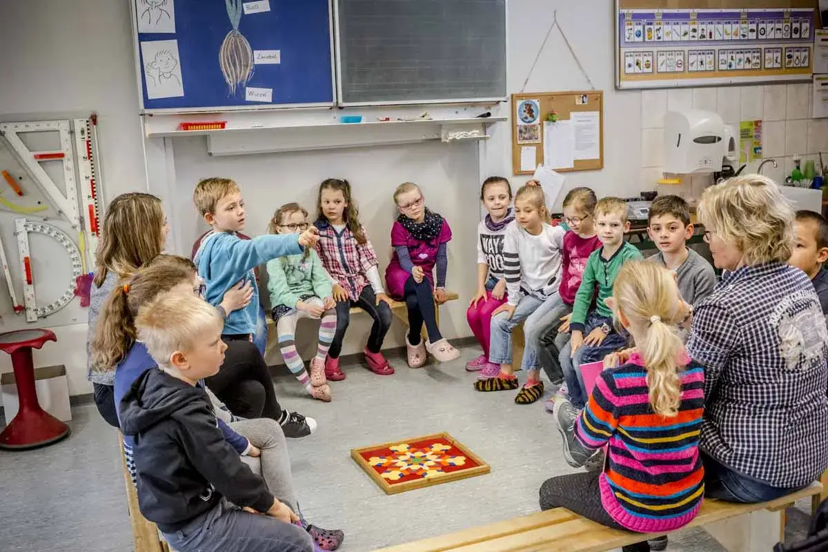 Erste Klasse in Niedersachsen 2026: Kinder sitzen im Kreis, ein Junge zeigt auf ein Spiel.