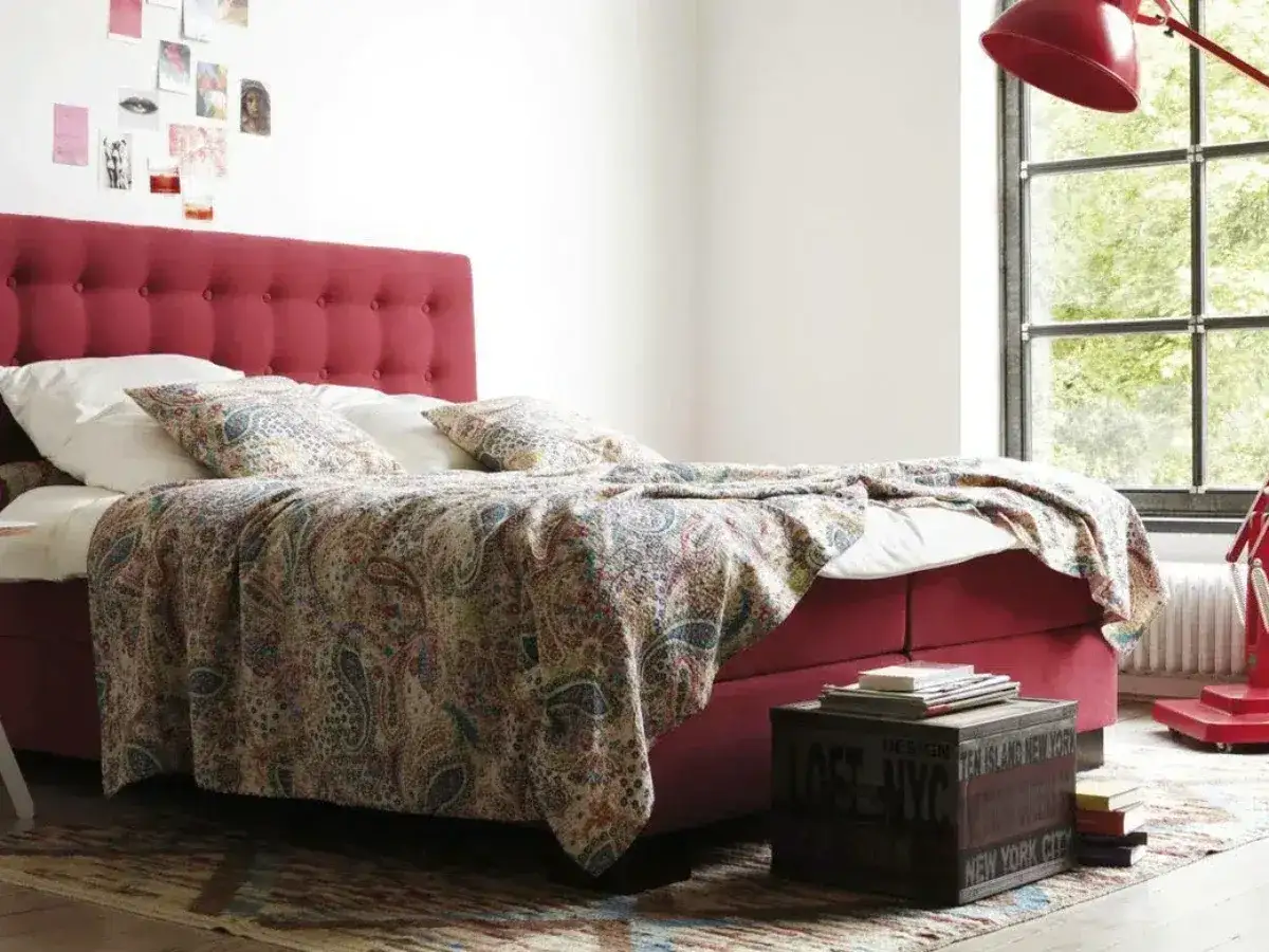 Rotes Boxspringbett mit gemustertem Überwurf und Kissen. Ideal für Allergiker, die Wert auf Stil legen.