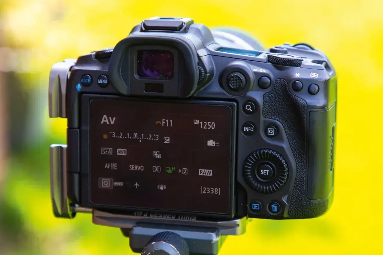 Tył aparatu z ekranem pokazującym ustawienia, w tym przysłonę F11 i ISO 1250. Widoczny jest też wskaźnik bracketing ostrości.