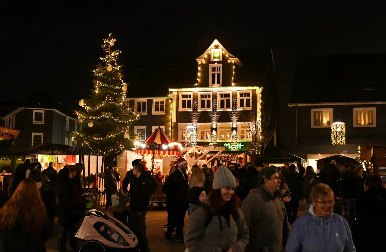 Menschen genie&szlig;en den stimmungsvollen Radevormwald Weihnachtsmarkt bei Nacht, beleuchtet von einem festlichen Baum und Lichtern.