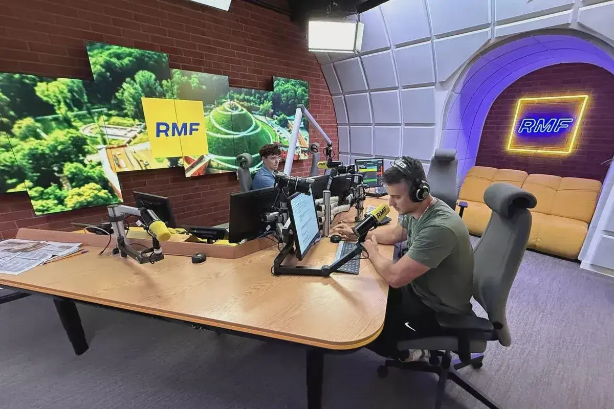 Dwóch prezenterów w studiu RMF FM przygotowuje się do audycji. Na ścianie wisi logo RMF.