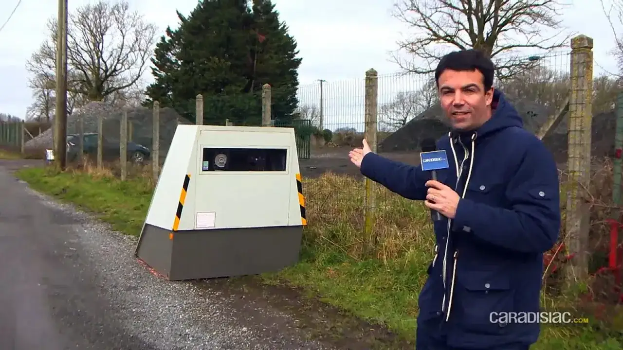 Un journaliste pr&eacute;sente un radar leurre, une fausse cabine de contr&ocirc;le de vitesse install&eacute;e sur le bord de la route pour dissuader les automobilistes de d&eacute;passer la limite.