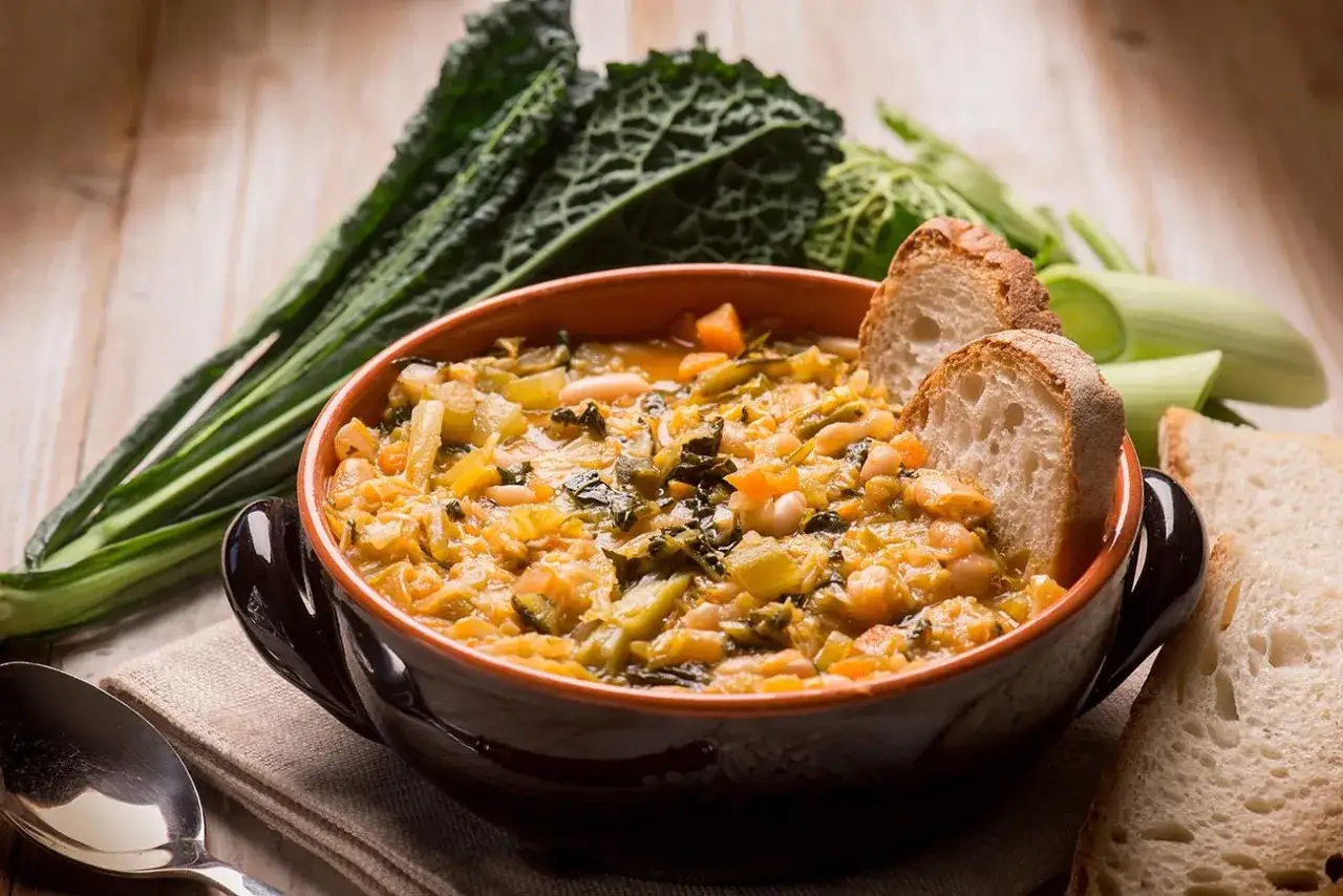 Una ciotola di ribollita fumante, ricca di verdure e fagioli, con fette di pane tostato.