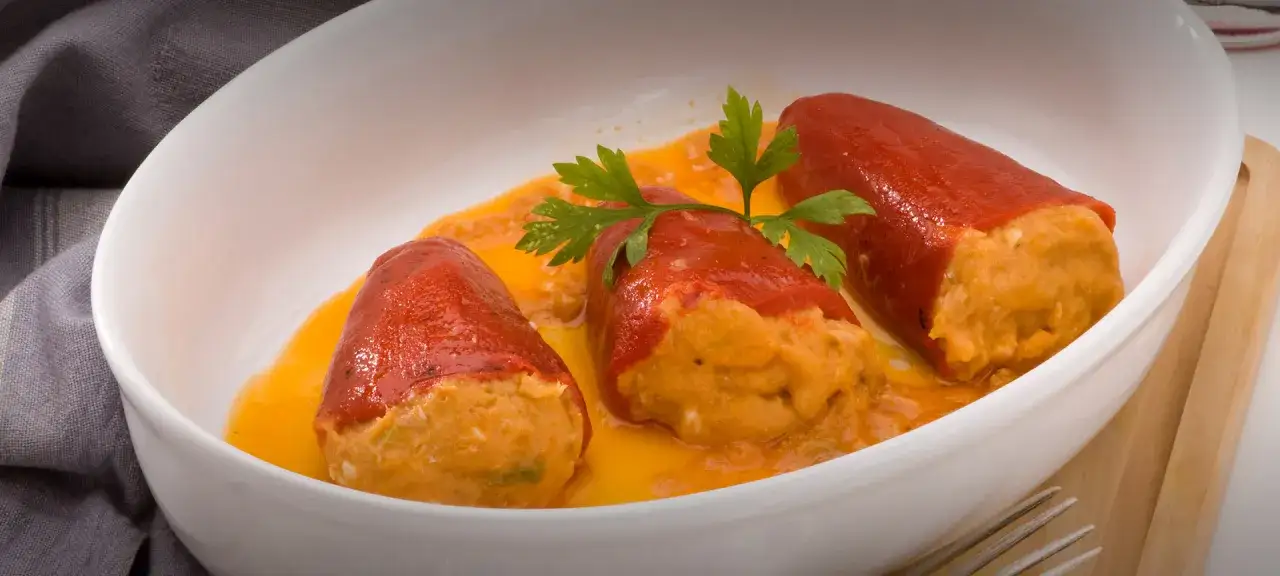 Tres pimientos del piquillo rellenos de una mezcla sabrosa, bañados en una salsa naranja y decorados con perejil fresco.