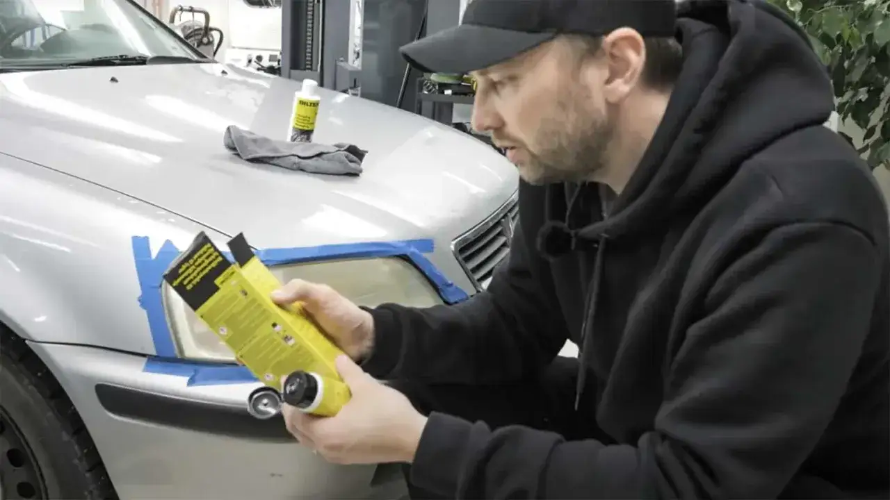 Man förbereder polering strålkastare biltema. En flaska med produkt och trasa ligger på bilen.