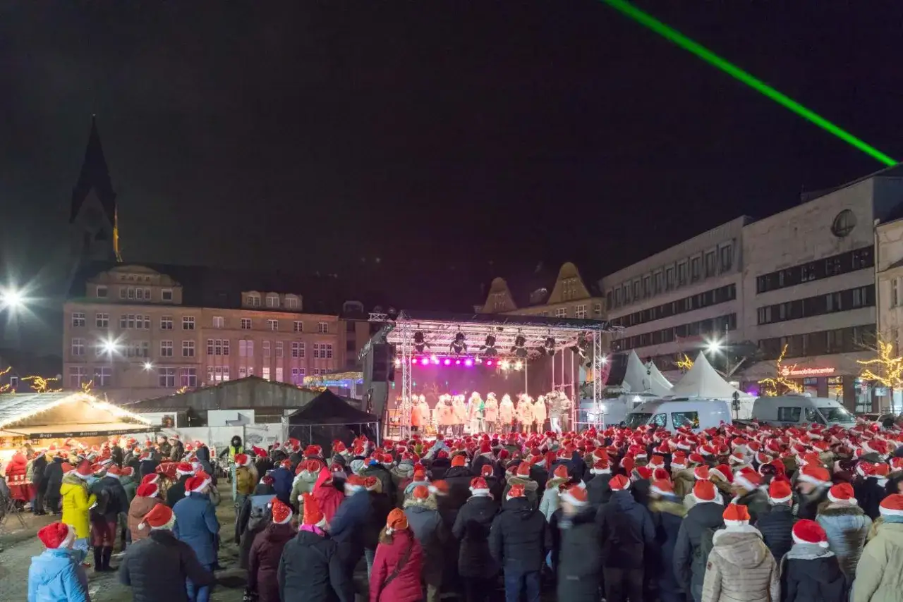 Große Menschenmenge mit Weihnachtsmützen auf dem Castrop Rauxel Weihnachtsmarkt, während eine Gruppe auf der Bühne singt.