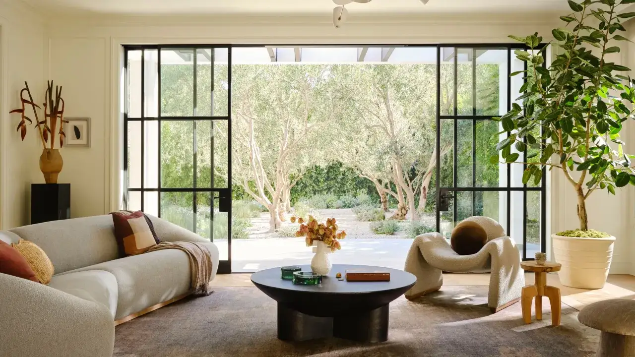 Salones elegantes con sof&aacute;s curvos y sill&oacute;n acogedor, conectados a un jard&iacute;n con olivos a trav&eacute;s de puertas correderas de cristal.