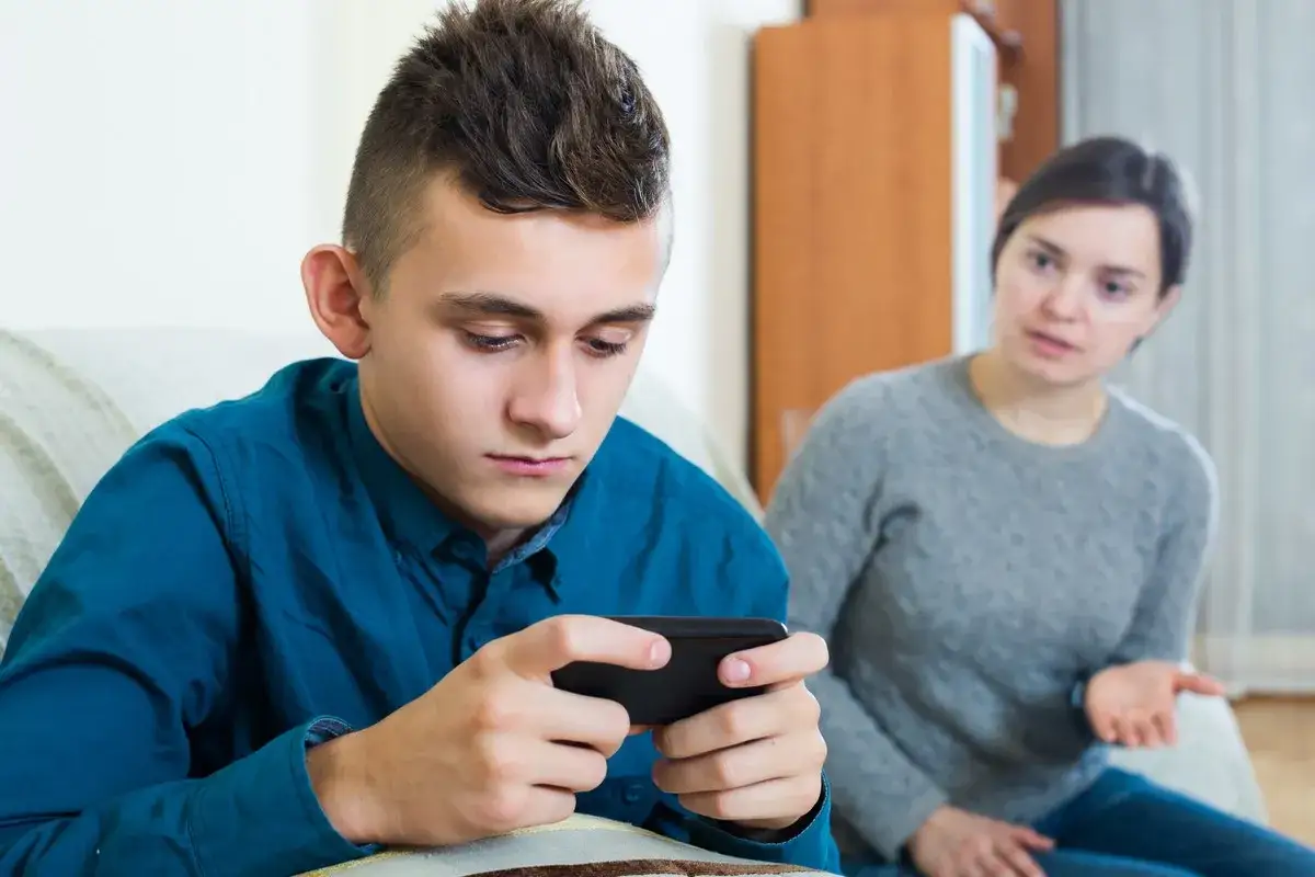 Un adolescent concentr&eacute; sur son t&eacute;l&eacute;phone, sa m&egrave;re lui parle. Elle envisage peut-&ecirc;tre de bloquer internet sur son t&eacute;l&eacute;phone.
