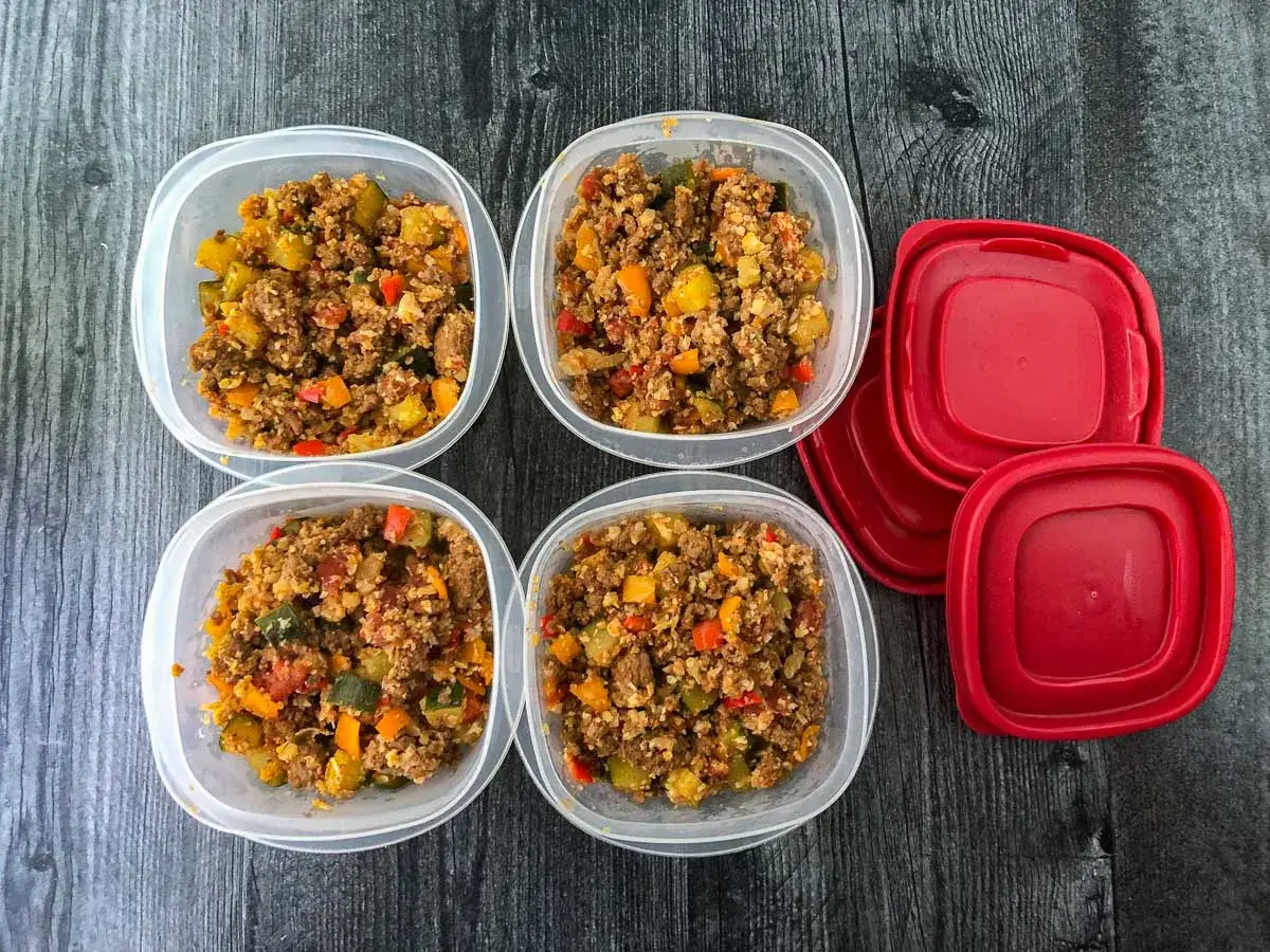 Vier Behälter mit leckeren low carb mahlzeiten, gefüllt mit Hackfleisch und Gemüse. Rote Deckel liegen daneben.