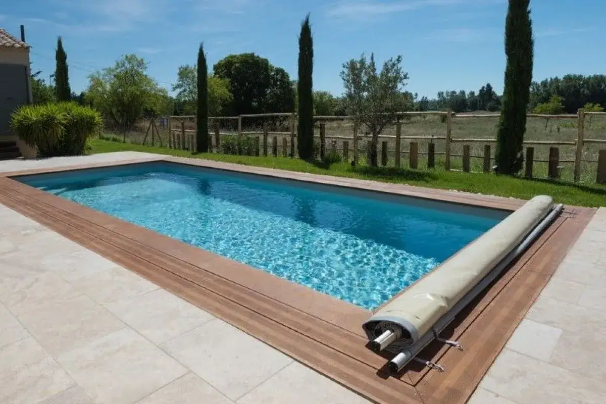 Piscine rectangulaire avec couverture enroulée, un élément clé pour la sécurité piscine réglementation. Le bois et les dalles créent un espace moderne.