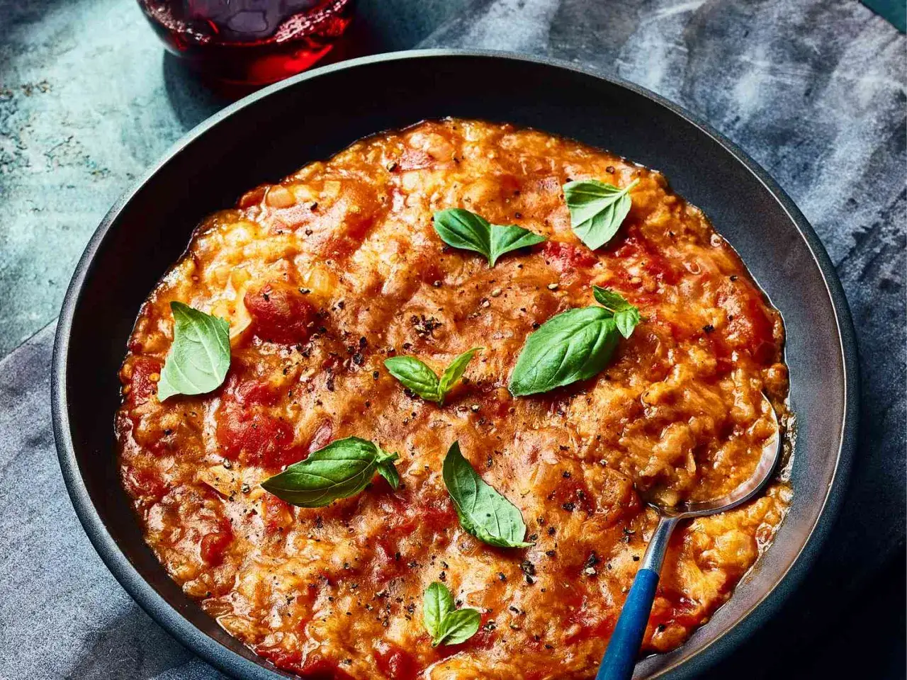 Un plat réconfortant de pappa al pomodoro, garni de feuilles de basilic frais et de poivre noir, servi dans un bol sombre.