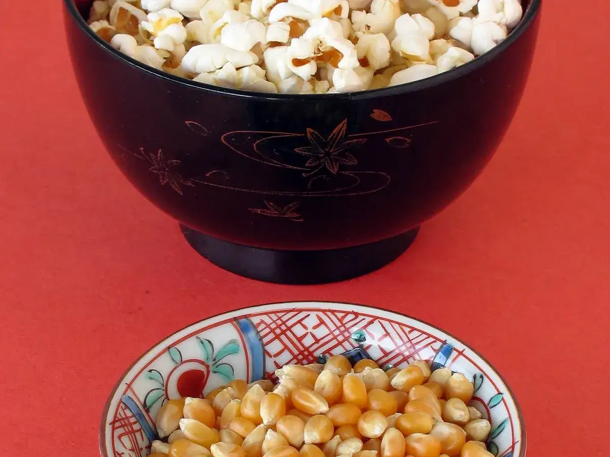 Un bol de pop corn maison, prêt à être dégusté, côtoie un petit bol rempli de grains de maïs.
