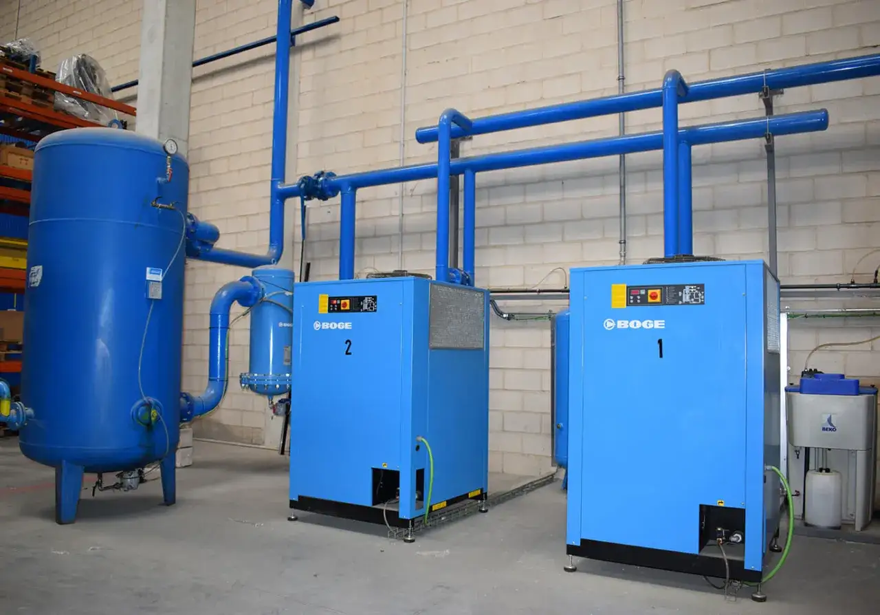 En la sala de compresores, dos unidades BOGE azules, etiquetadas 1 y 2, junto a un gran tanque azul y tuberías.