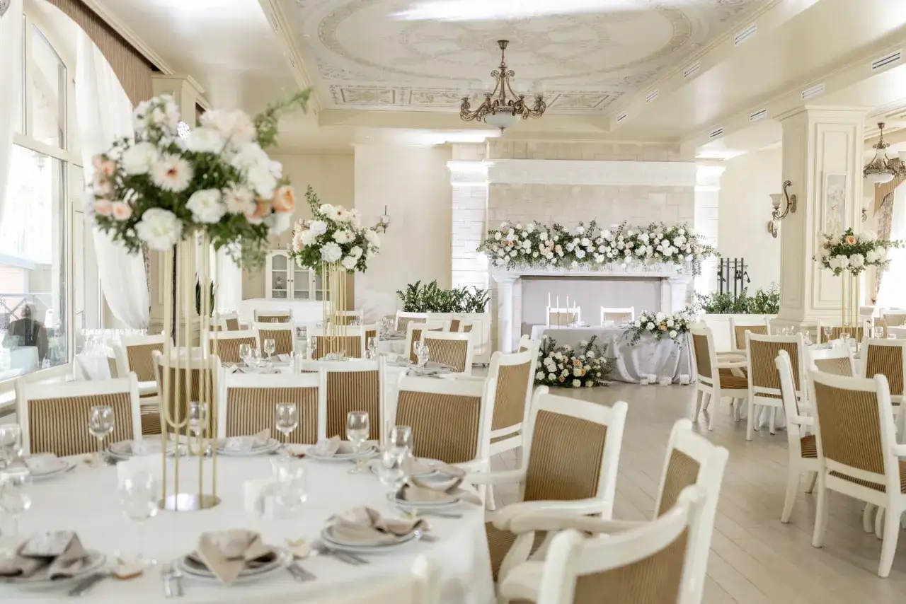 Elegancka sala weselna z białymi stołami i krzesłami, udekorowana kwiatami. Zastanawiasz się, ile kosztuje 18 na 30 osób?