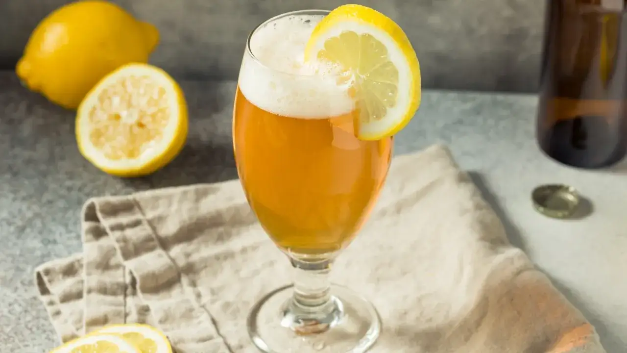 Verre de bière ambrée avec une tranche de citron, accompagné de citrons frais et d'une bouteille. Un nom de bière citron parfait pour l'été.
