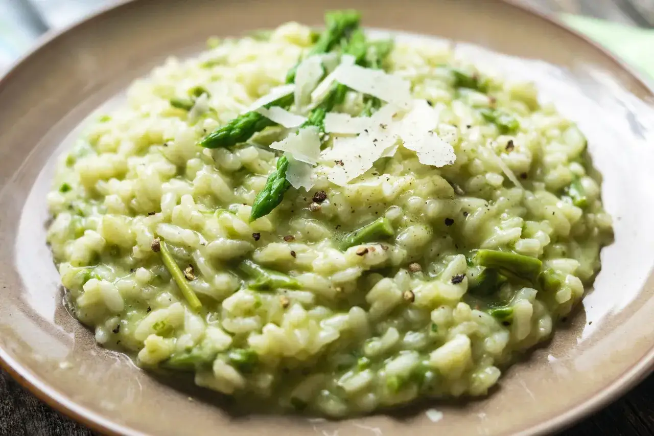 Kremowe, **prawdziwe włoskie risotto** z zielonymi szparagami i płatkami parmezanu, posypane świeżo mielonym pieprzem.